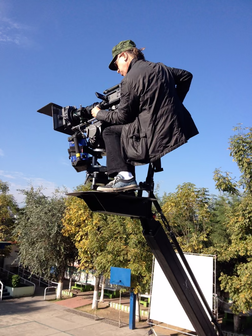 Un camarógrafo en la silla de una grúa con la cámara, contra el cielo azul