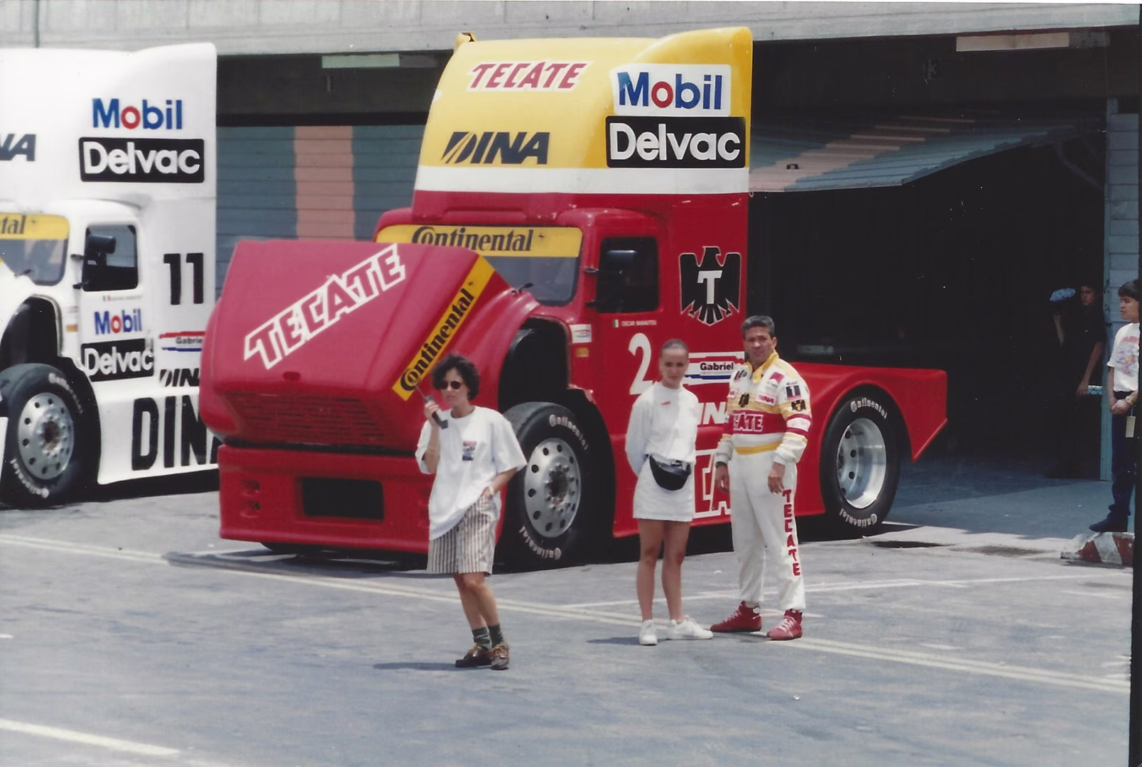 Un tractocamión de carreras rojo en los pits, con tres personas al frente