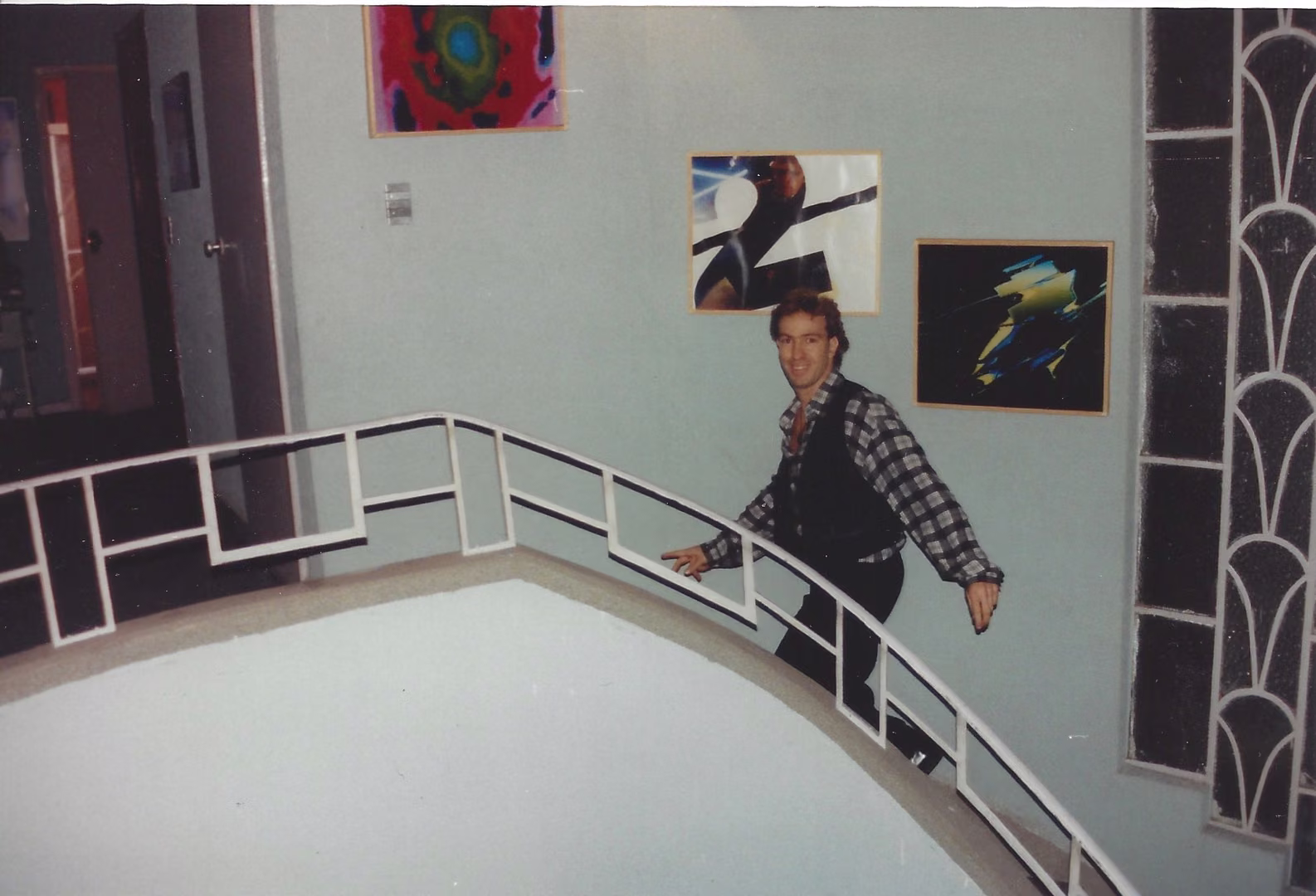 Benny Corral baja una escalera curva blanca; en la pared, cuadros de colores